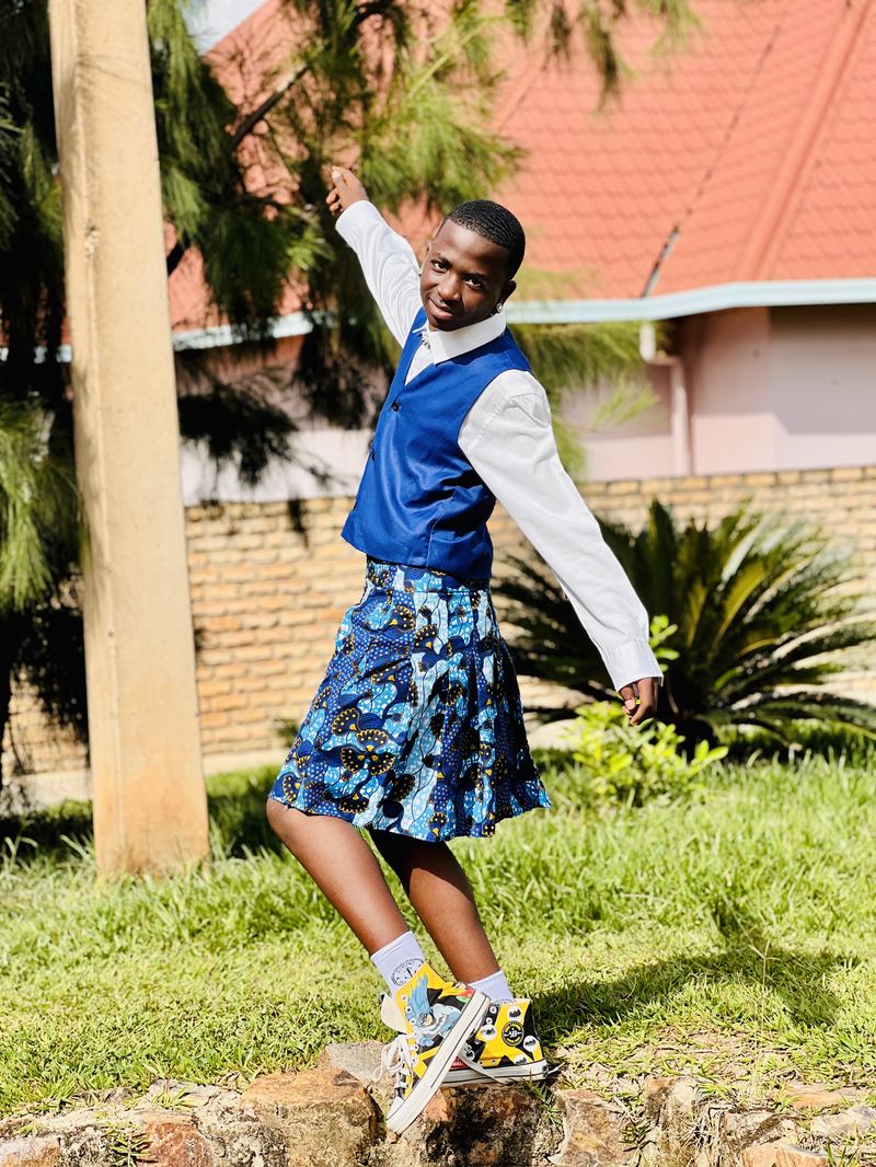 A young CCF dancer mid-pose in vest and African-print kilt.