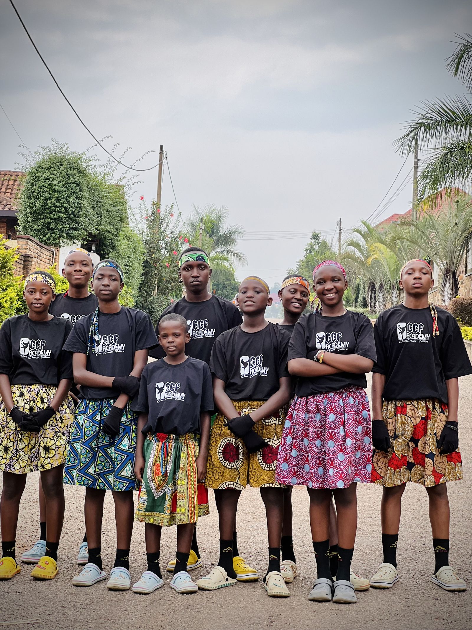 The CCF crew lined up on a Kigali street in black CCF Academy t-shirts and African-print kilts.